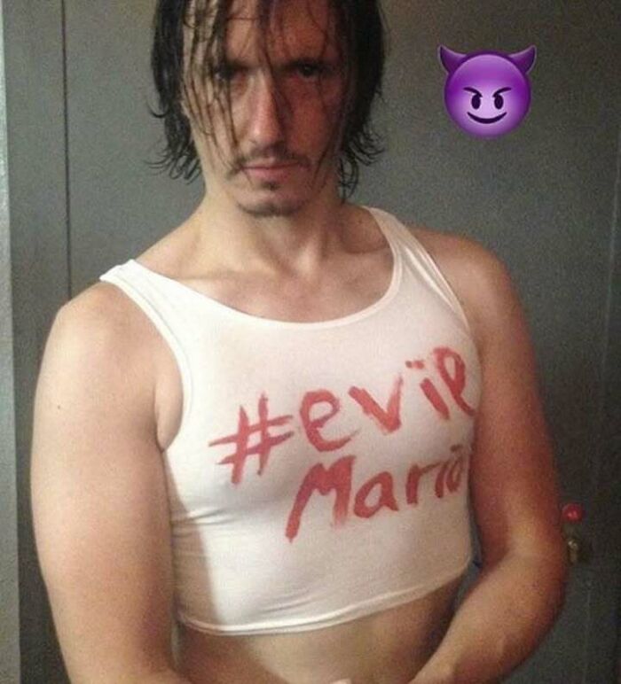 A man wearing a white crop top with #evil Mario written on it, resembling a fever dream meme.