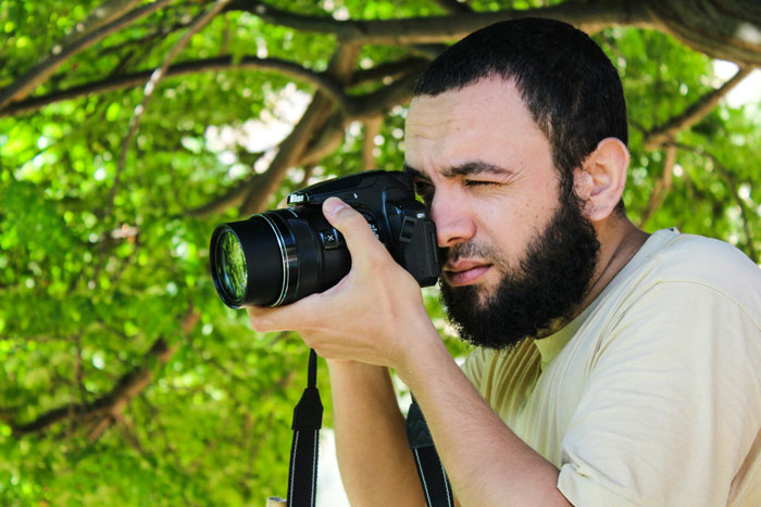 Man with beard taking photo with camera under green tree