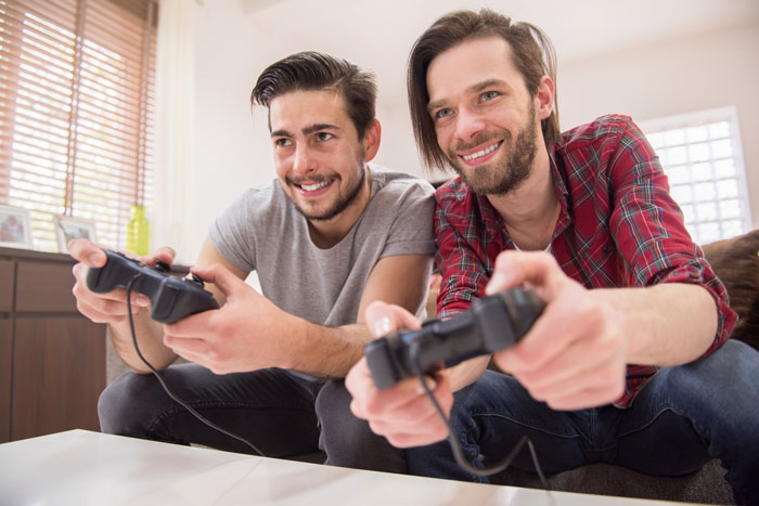 Two happy men playing video games on a couch, representing relationship dynamics. Two happy men playing video games on a couch, representing relationship dynamics.