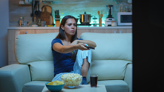 A woman on a couch watching TV, with popcorn and chips, reflecting a picky eater girlfriend's relationship dynamics. A woman on a couch watching TV, with popcorn and chips, reflecting a picky eater girlfriend's relationship dynamics.