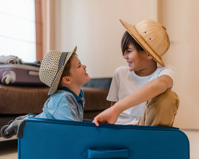 Two boys wearing hats smiling and playing with suitcase representing parenting and travel challenges Two boys wearing hats smiling and playing with suitcase representing parenting and travel challenges