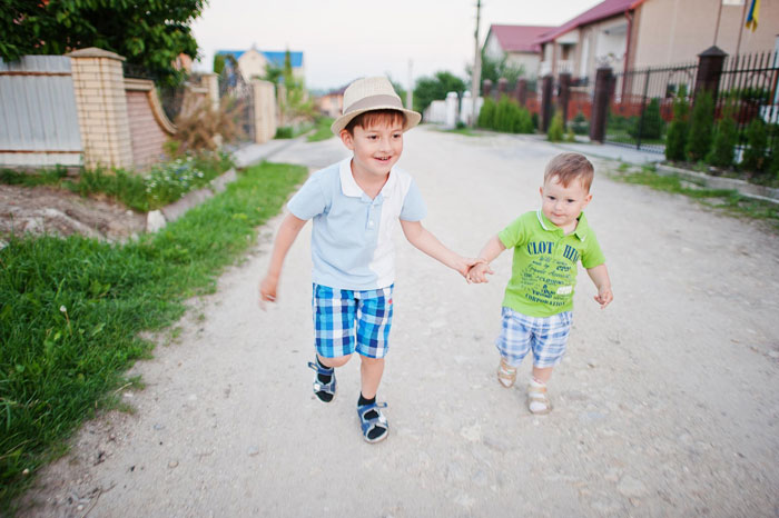 Two young boys holding hands running outside near houses Two young boys holding hands running outside near houses