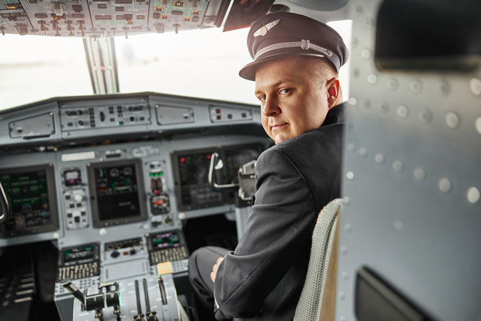 Pilot in uniform sitting in airplane cockpit looking back Pilot in uniform sitting in airplane cockpit looking back