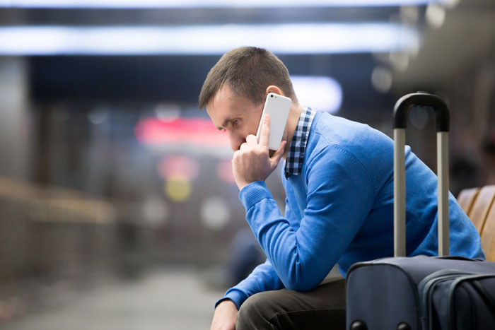Man in blue sweater sitting at airport talking on phone with luggage beside him Man in blue sweater sitting at airport talking on phone with luggage beside him