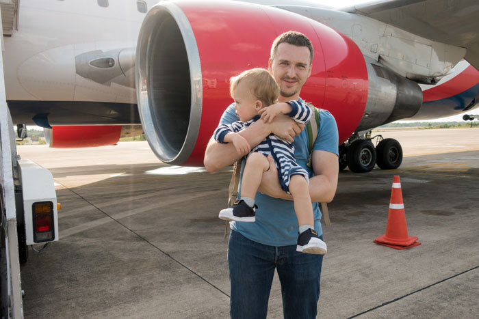 Father holding toddler near airplane engine on airport tarmac Father holding toddler near airplane engine on airport tarmac