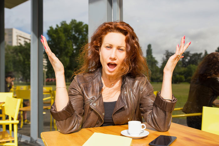 A frustrated pregnant woman working in a pub with her hands raised in exasperation.