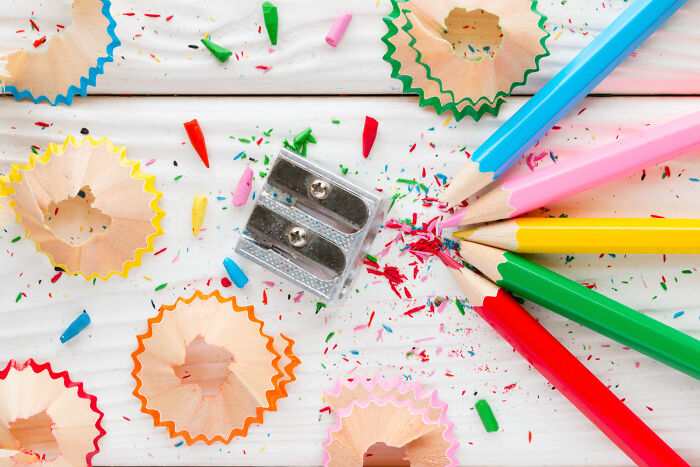 Sharpener and colorful sharpened pencils with shavings on white table