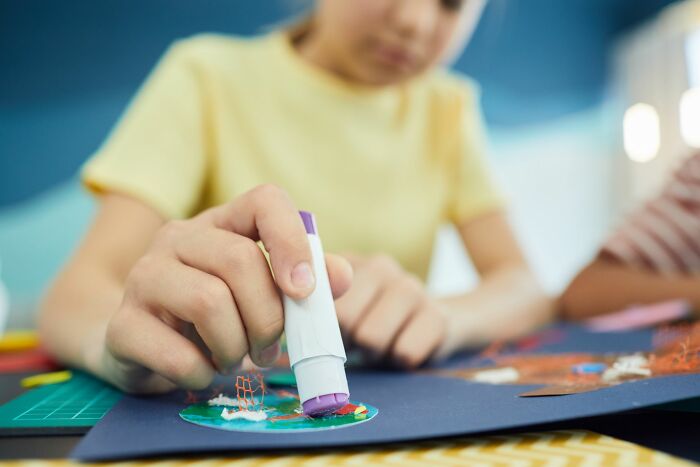 Primary kid using glue stick for school craft project indoors