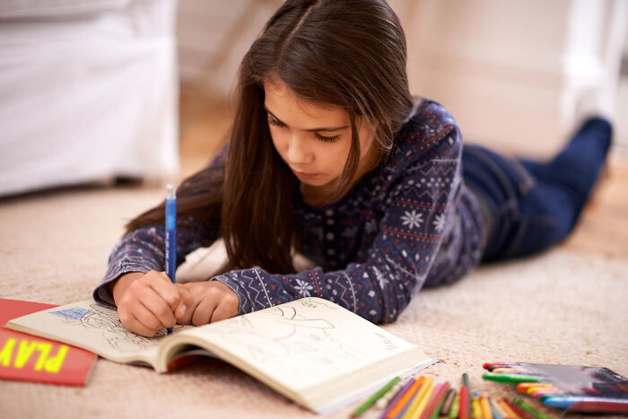 Primary girl drawing in coloring book on floor