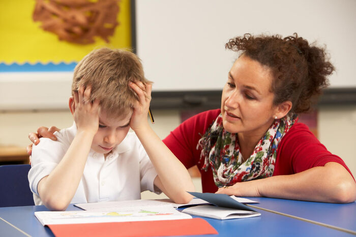Teacher comforting stressed primary boy struggling with schoolwork