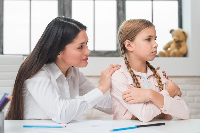 Teacher consoling upset primary school girl with arms crossed