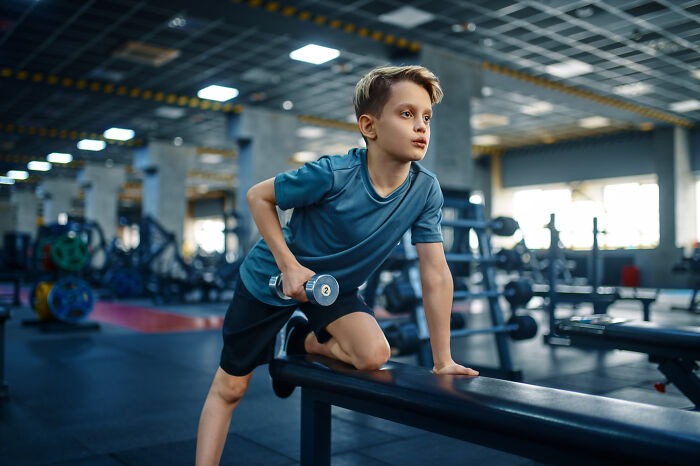 Primary child lifting dumbbell in gym setting
