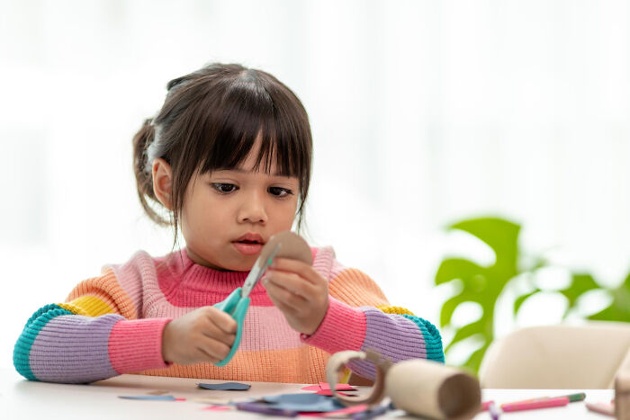 Young girl focused cutting paper with scissors in classroom crafting activity