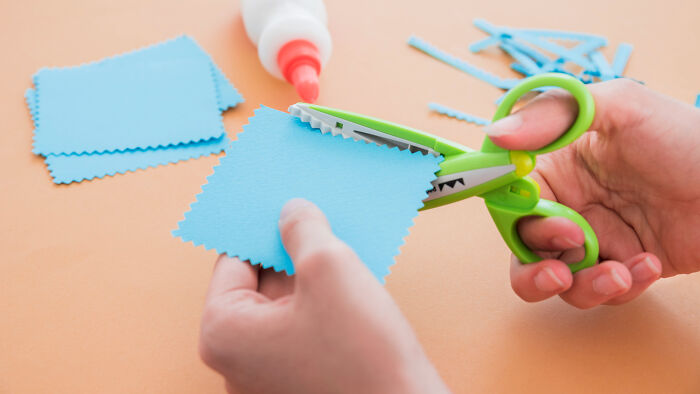 Hands cutting blue paper with craft scissors for a primary school project