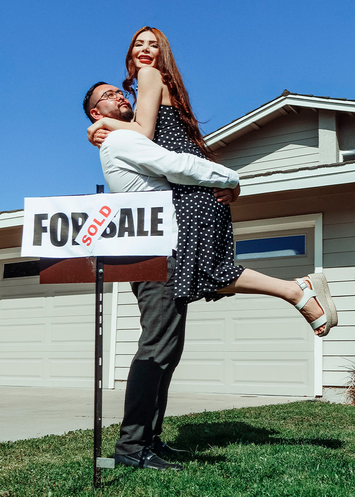 A couple celebrating in front of a home with a SOLD sign, highlighting the homeowners private investigator warning.