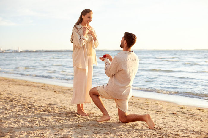 Man kneeling on beach proposing to woman by the sea