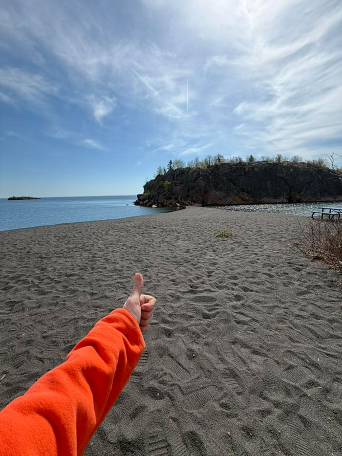 Person giving thumbs up on empty beach with rocky outcrop