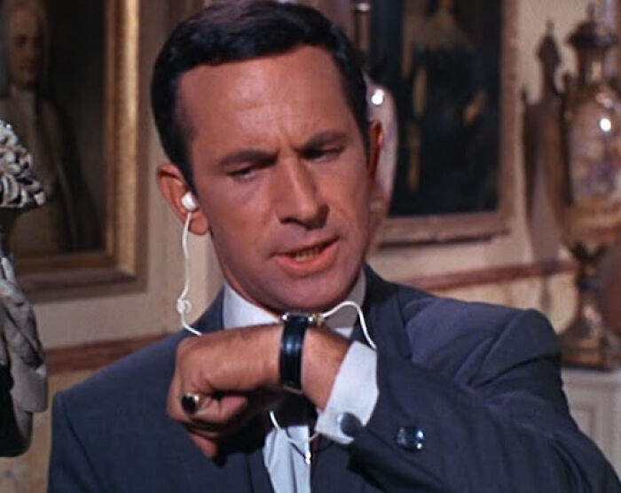 A man in a suit checking his watch, with an earbud, taking you way back and reminding you how old you are.