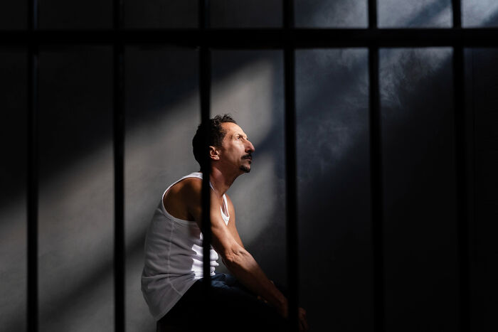 Man sitting behind bars in shadow, reflecting consequences of a psychopath