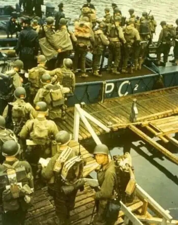Historical photos: Soldiers in uniform with helmets and gear board a transport boat at a wooden pier.