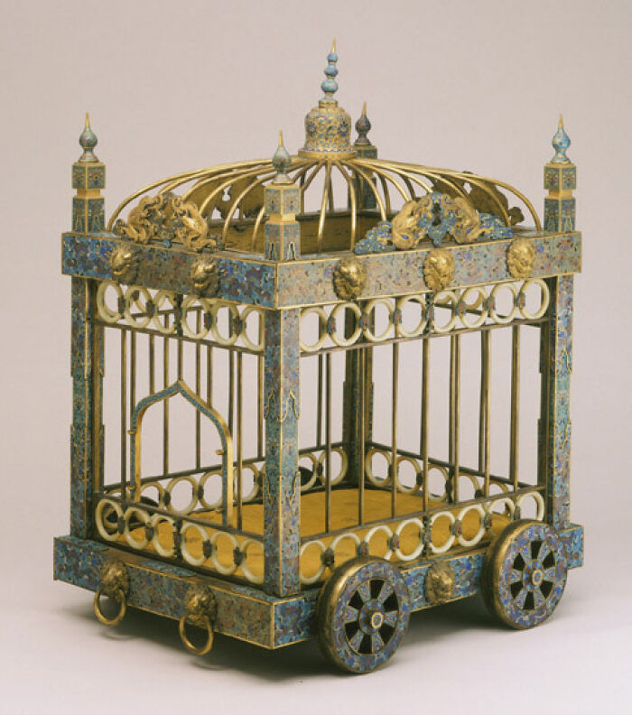 An ornate, intact birdcage with gold and blue details, on wheels, showcasing interesting objects still intact.