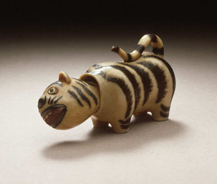 A small, intact ceramic tiger figurine with black stripes and an open mouth, an interesting object.