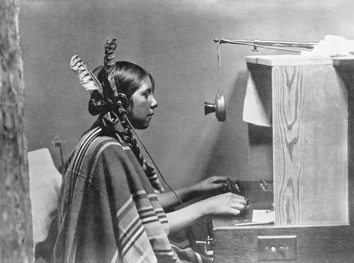 A vintage photo of a woman with braided hair and feathers, using a switchboard, an interesting photo still intact.