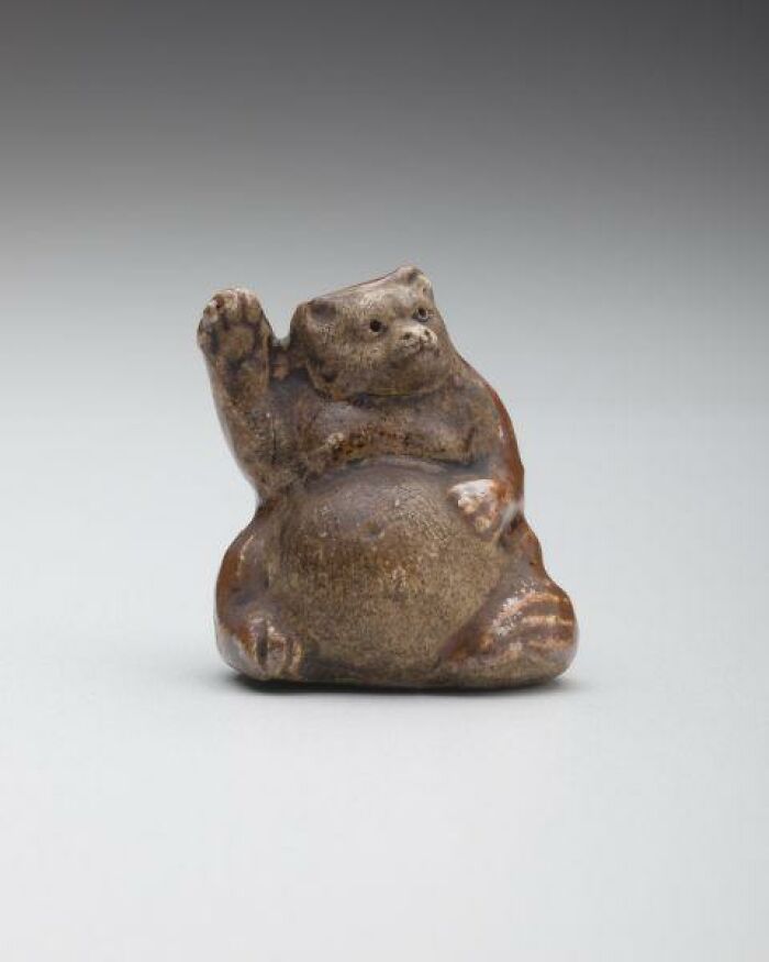 Intact after years, a small, brown, ceramic animal figurine with one paw raised, resembling a beckoning creature.