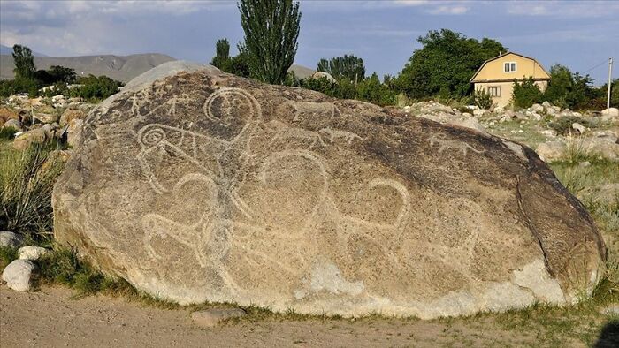 Intact after years, a large rock adorned with ancient petroglyphs, depicting animals and symbols in an outdoor setting.