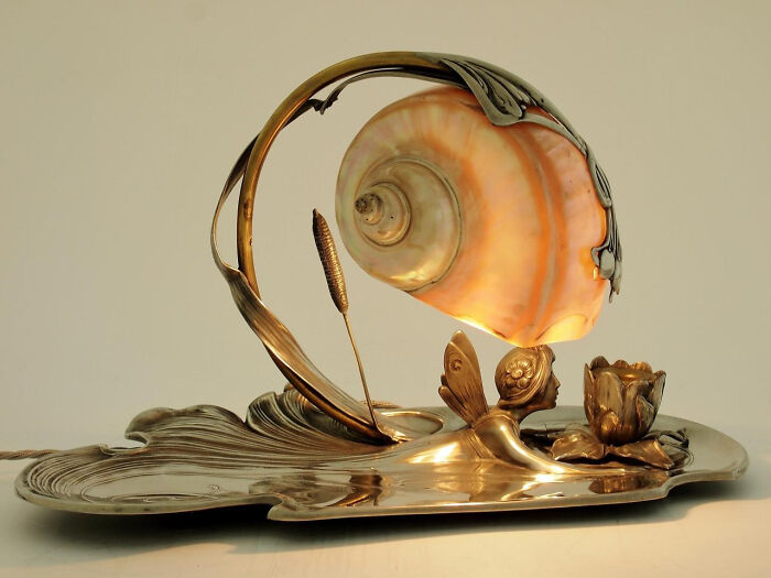 A stunning Art Nouveau lamp with a seashell shade and a fairy figurine, an intact object from many years ago.