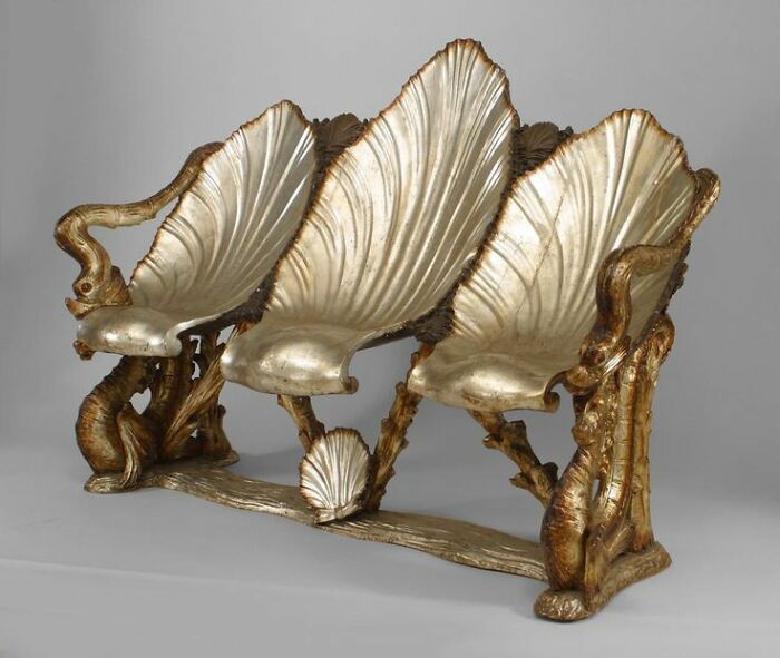 Intact after years, a gilded shell-shaped bench with intricate details and three seats stands majestically.