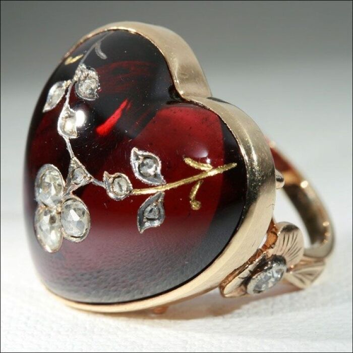 A beautiful gold ring with a large red heart-shaped gem adorned with delicate diamonds and leaves, an intact interesting object.