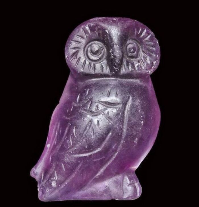 A small, purple, carved amethyst owl figurine, perfectly intact and showing its intricate details, an interesting object.
