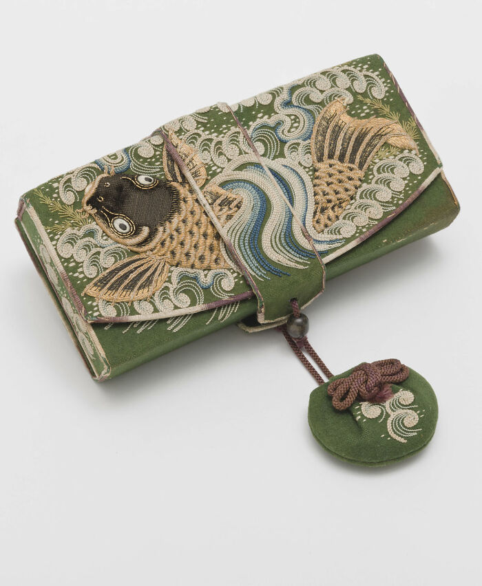 A remarkably intact green embroidered pouch featuring a detailed goldfish design, secured with a tie and a circular charm, showcasing interesting objects.