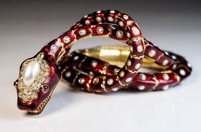A close-up of an ornate red and gold snake-shaped bracelet with pearls and jewels, an interesting object still intact.