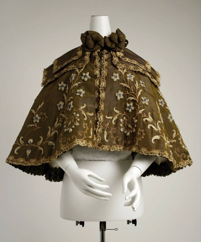 An elaborately embroidered silk cape with floral patterns, perfectly intact after many years, displayed on a mannequin.