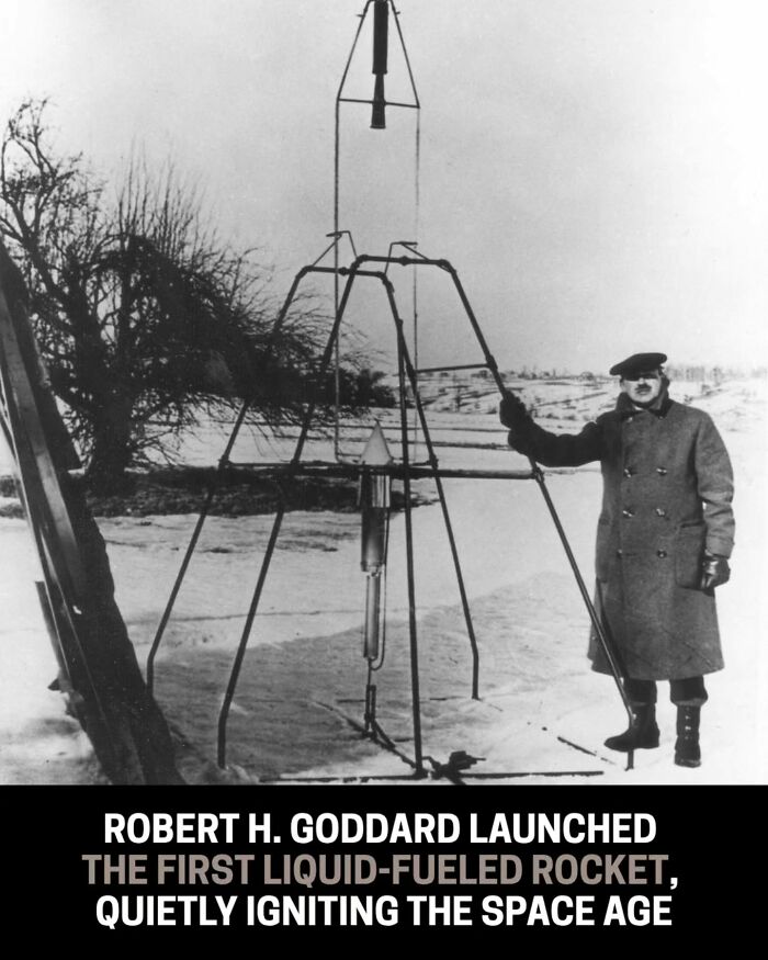 Black and white historical photo of Robert H. Goddard with the first liquid-fueled rocket he launched, in a snowy field.