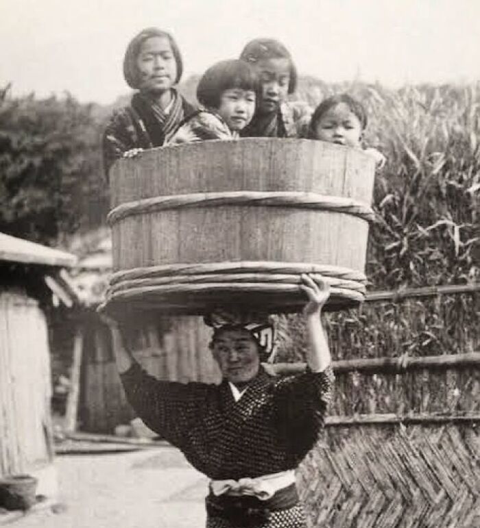 A woman carrying a large wooden bucket with four children inside on her head, a rare historical photo.