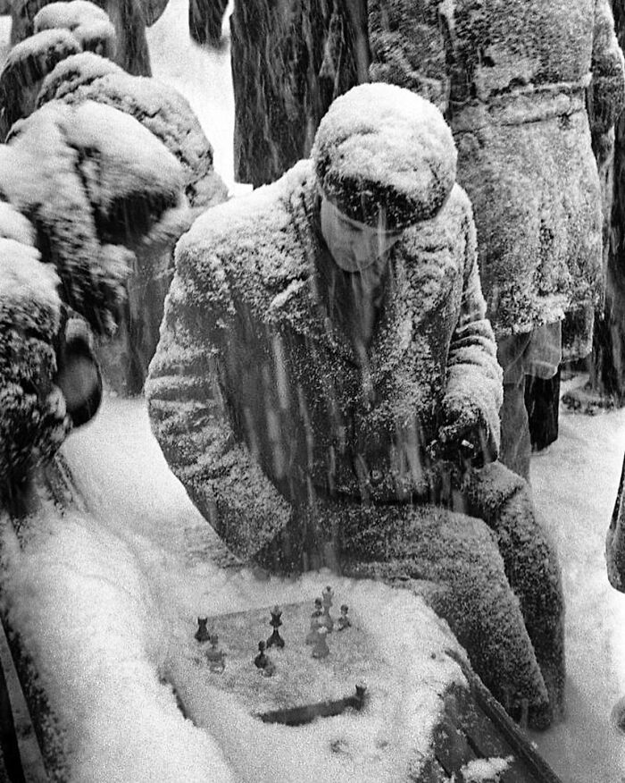 A man playing chess outside in the snow, covered in snowflakes, in a rare historical photo.