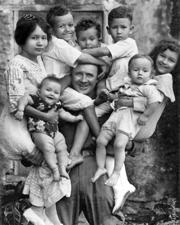 A man is surrounded by seven children in a warm embrace, a heartwarming subject from interesting historical photos.