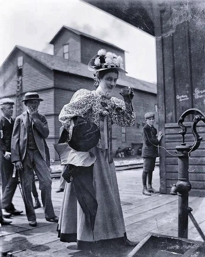 A well-dressed woman sips from a cup near a water pump, captured in interesting historical photos from an earlier era.