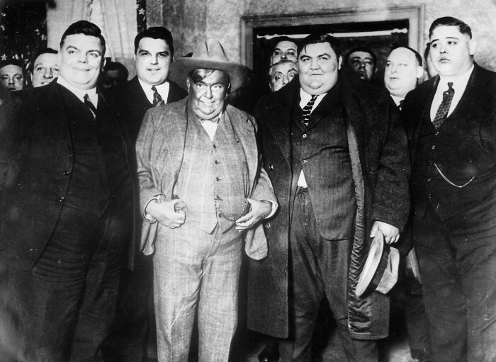 A group of men in suits, including one in a cowboy hat, pose for an interesting historical photo.