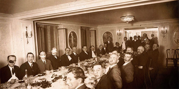 A long table of men in an interesting historical photo, many with bandages or unusual facial expressions.