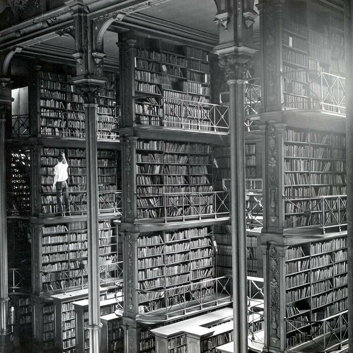 A vast, multi-tiered library filled with books, a librarian on a ladder, a rare historical photo of architecture.