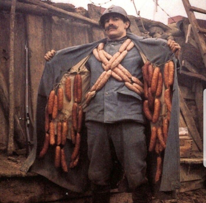 A soldier in uniform with a mustache, his coat open to reveal numerous sausages hanging inside, an interesting historical photo.
