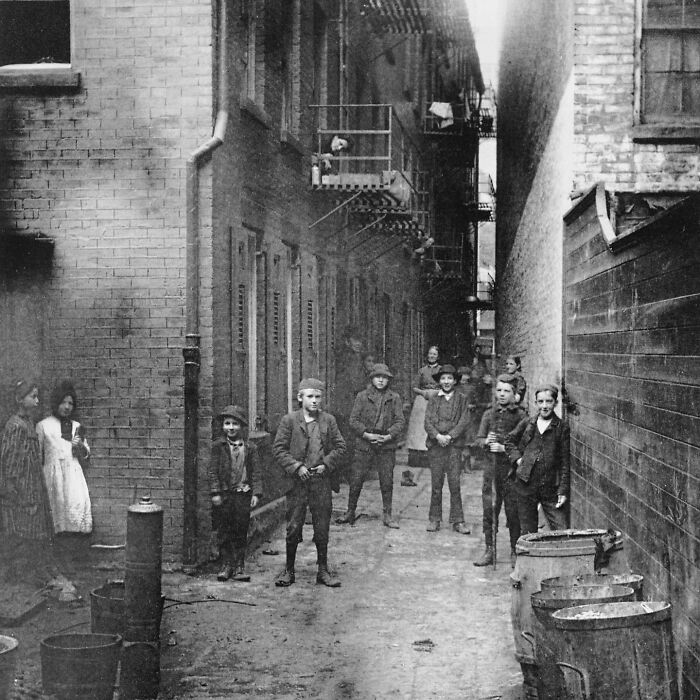 A group of children in a narrow, dirty alleyway surrounded by old brick buildings, an interesting historical photo.