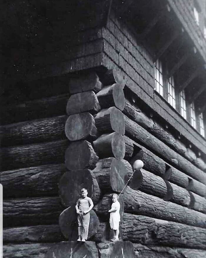 Two children with a balloon stand by a large log cabin, capturing a rare and interesting historical photo.