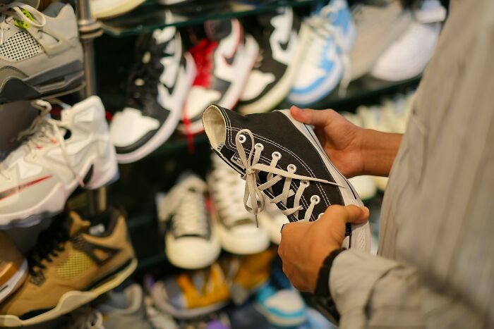 Person holding black sneaker in shoe store with various colorful shoes displayed