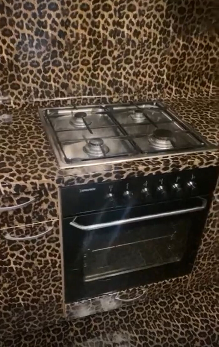 An unhinged real estate listing image of a kitchen with counter and walls covered in leopard print design.