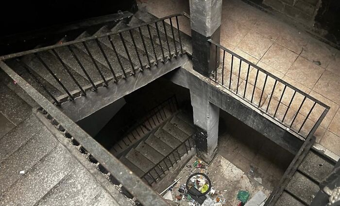 A dark, dirty, multi-level concrete staircase with debris, showcasing unhinged real estate listings.